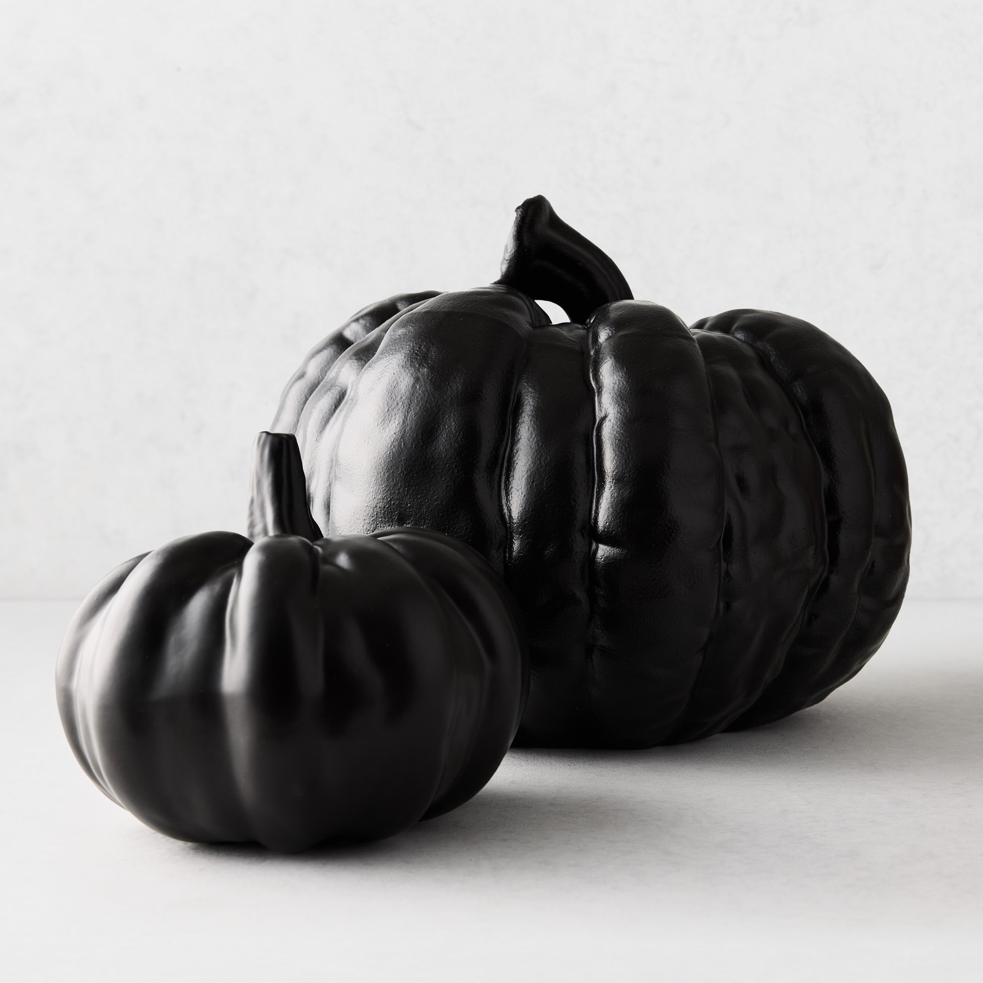 Two small matte black ceramic pumpkins with realistic ribbed textures on a white background.