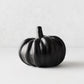 Small matte black ceramic pumpkin with a smooth, rounded ribbed design on a light background.