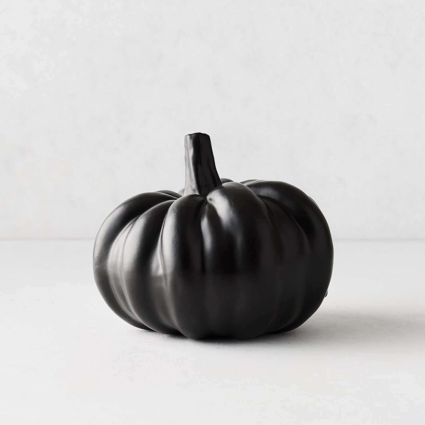Small matte black ceramic pumpkin with a smooth, rounded ribbed design on a light background.
