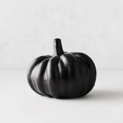 Small matte black ceramic pumpkin with a smooth, rounded ribbed design on a light background.