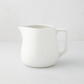 Small white ceramic milk pitcher with a simple, artisanal design.