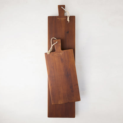 Two dark brown European pine serving planks, one small and one large, with rope hangers.