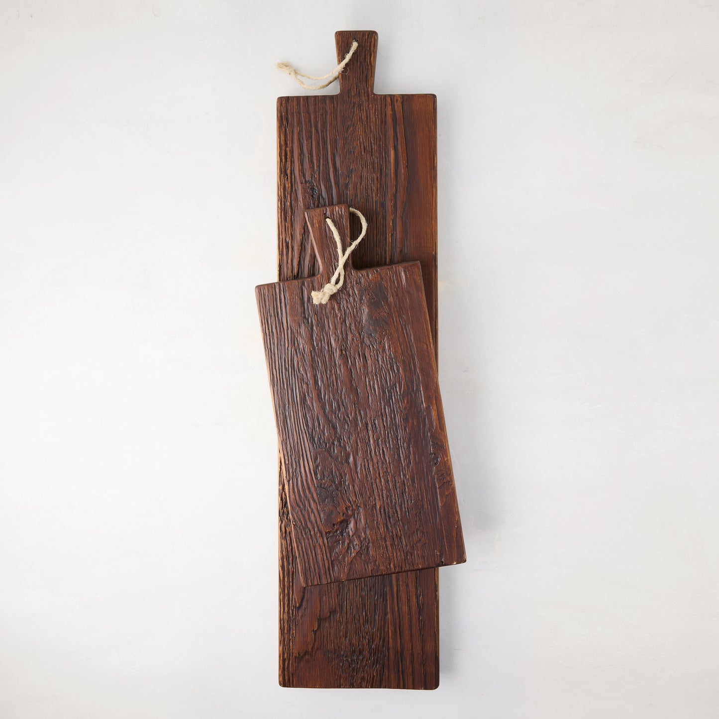 Two dark brown, rustic European pine wood serving planks with rope straps, one smaller, on a white background.