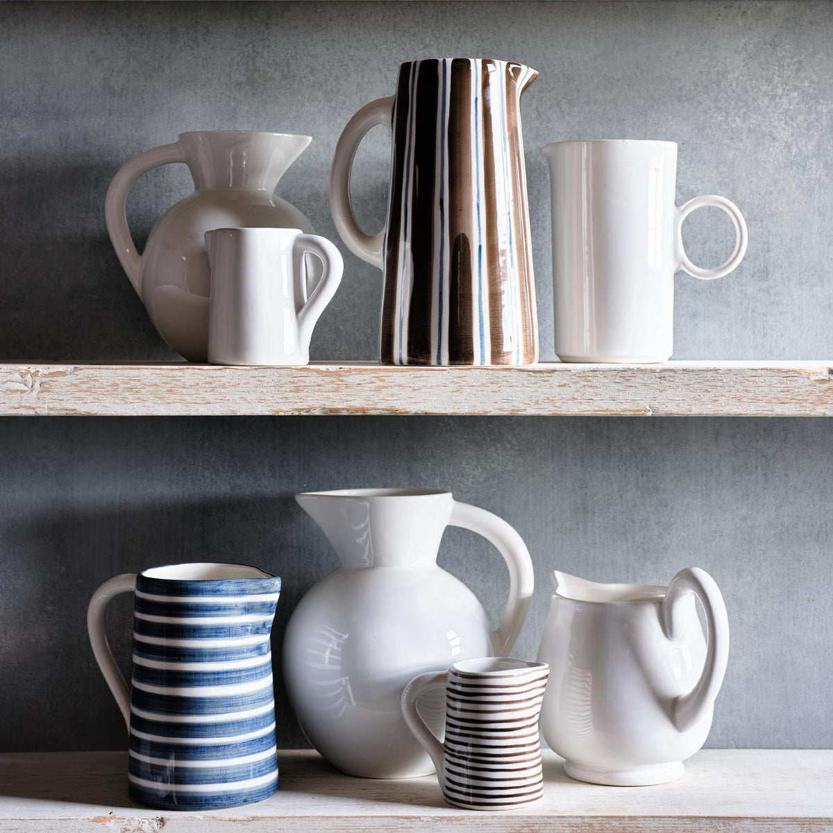 Small Salerno ceramic pitcher with white glaze and hand-painted thin brown stripes on a rustic wooden shelf.