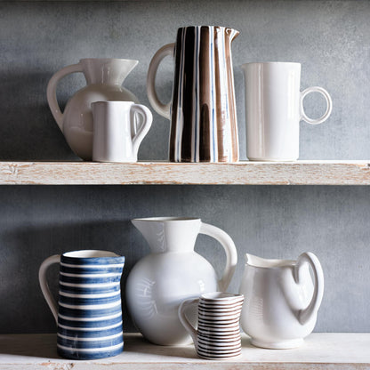 Small Salerno ceramic pitcher with white glaze and hand-painted thin brown stripes on a rustic wooden shelf.