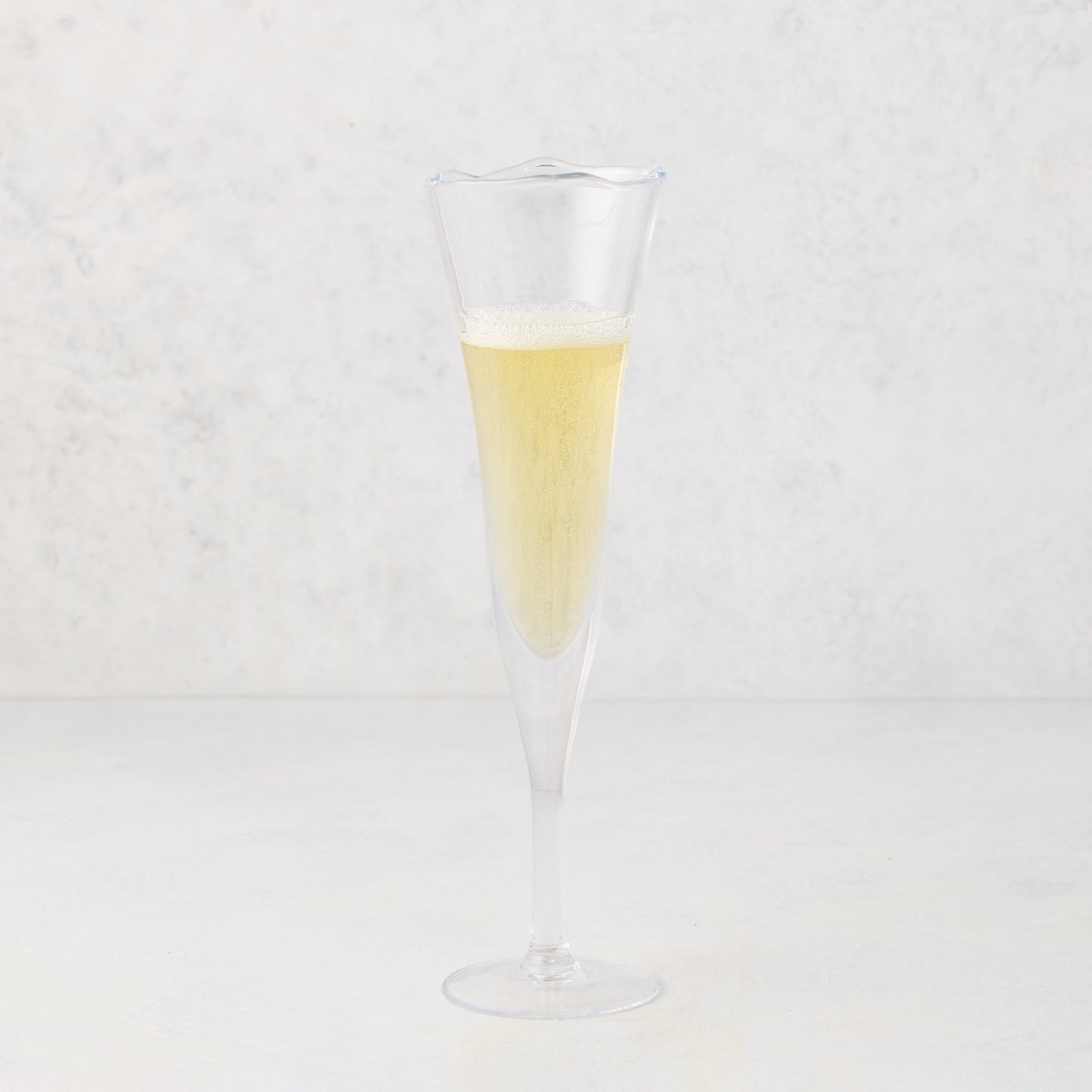 Small, clear scissor-cut glass champagne flute with a rippled rim, filled with bubbly champagne.