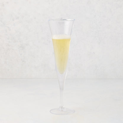 Small, clear scissor-cut glass champagne flute with a rippled rim, filled with bubbly champagne.