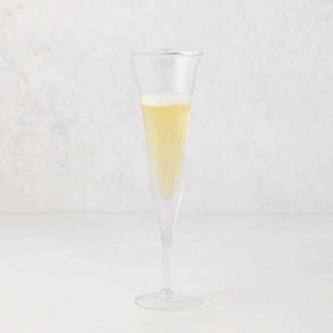 Small, clear scissor-cut glass champagne flute with a rippled rim, filled with bubbly champagne.