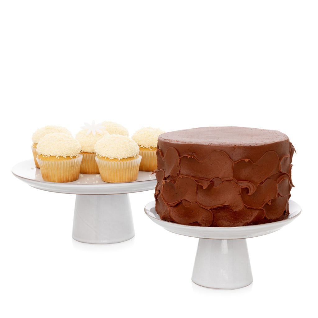 Two white terracotta cake stands. One holds a chocolate cake, the other holds six cupcakes.