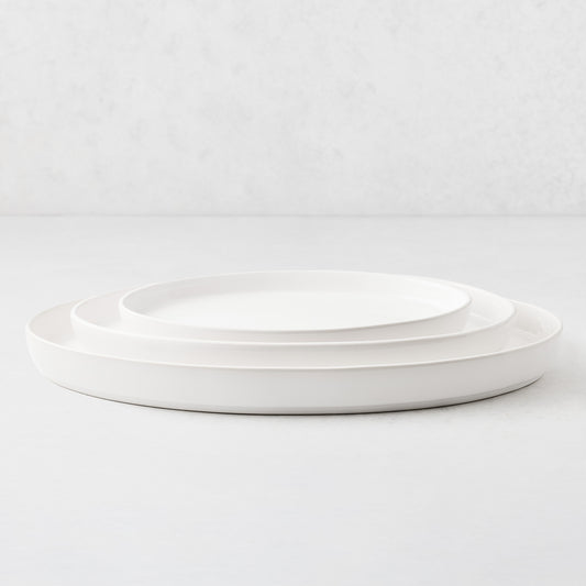 Set of three white stoneware oval nesting platters with a minimalist design on a white surface.