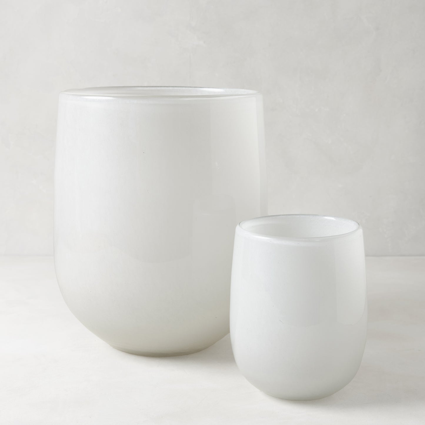 Two opaque white handblown glass barrel vases, one large and one small.