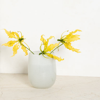 Small opaque white handblown glass barrel vase with yellow blooms.
