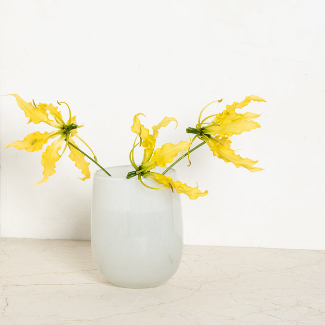 Small opaque white handblown glass barrel vase with yellow blooms.