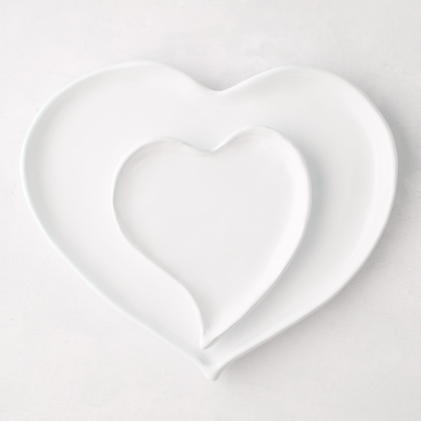 Two white ceramic heart-shaped dishes, one nested inside the other, on a light background.