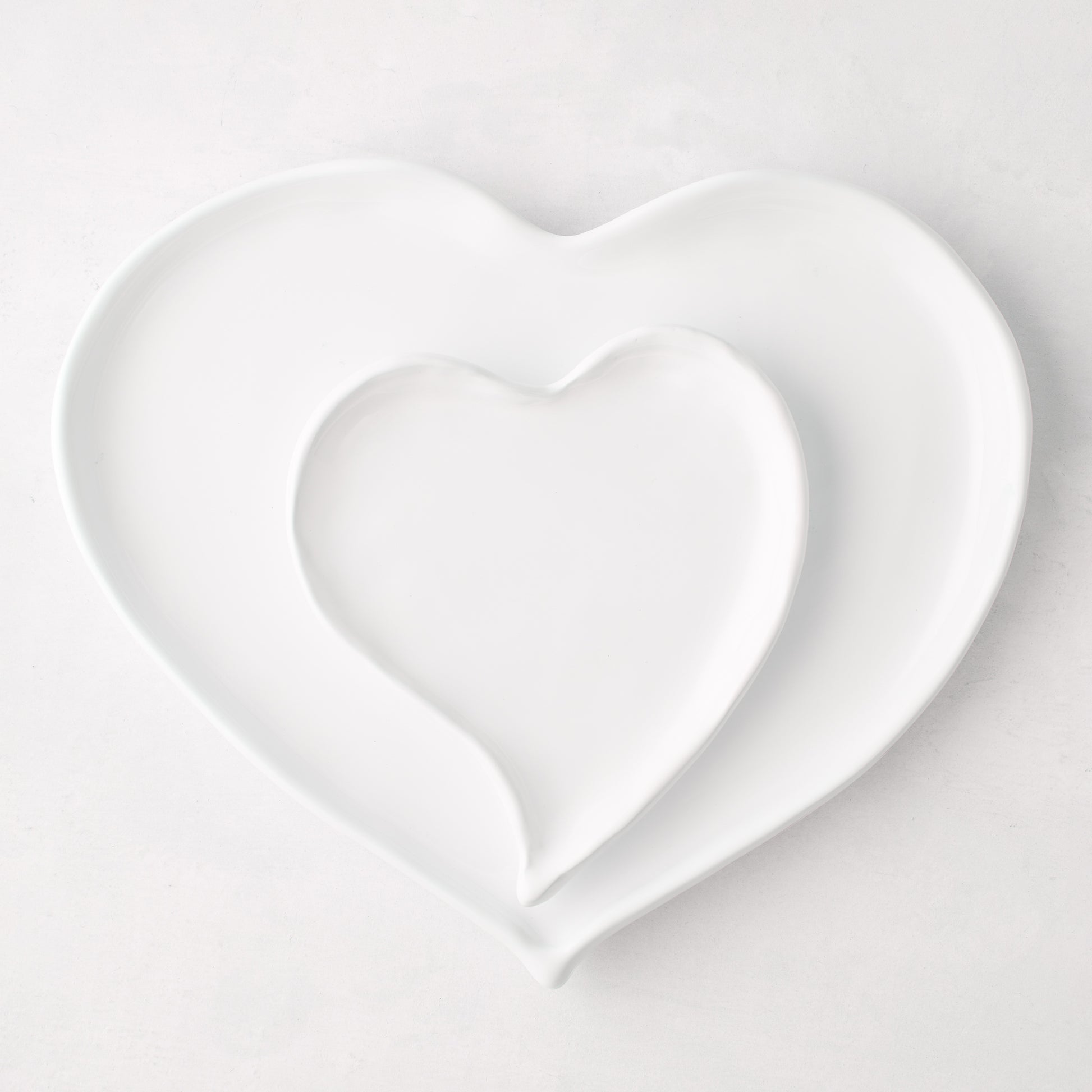 Two white ceramic heart-shaped dishes, one nested inside the other, on a light background.