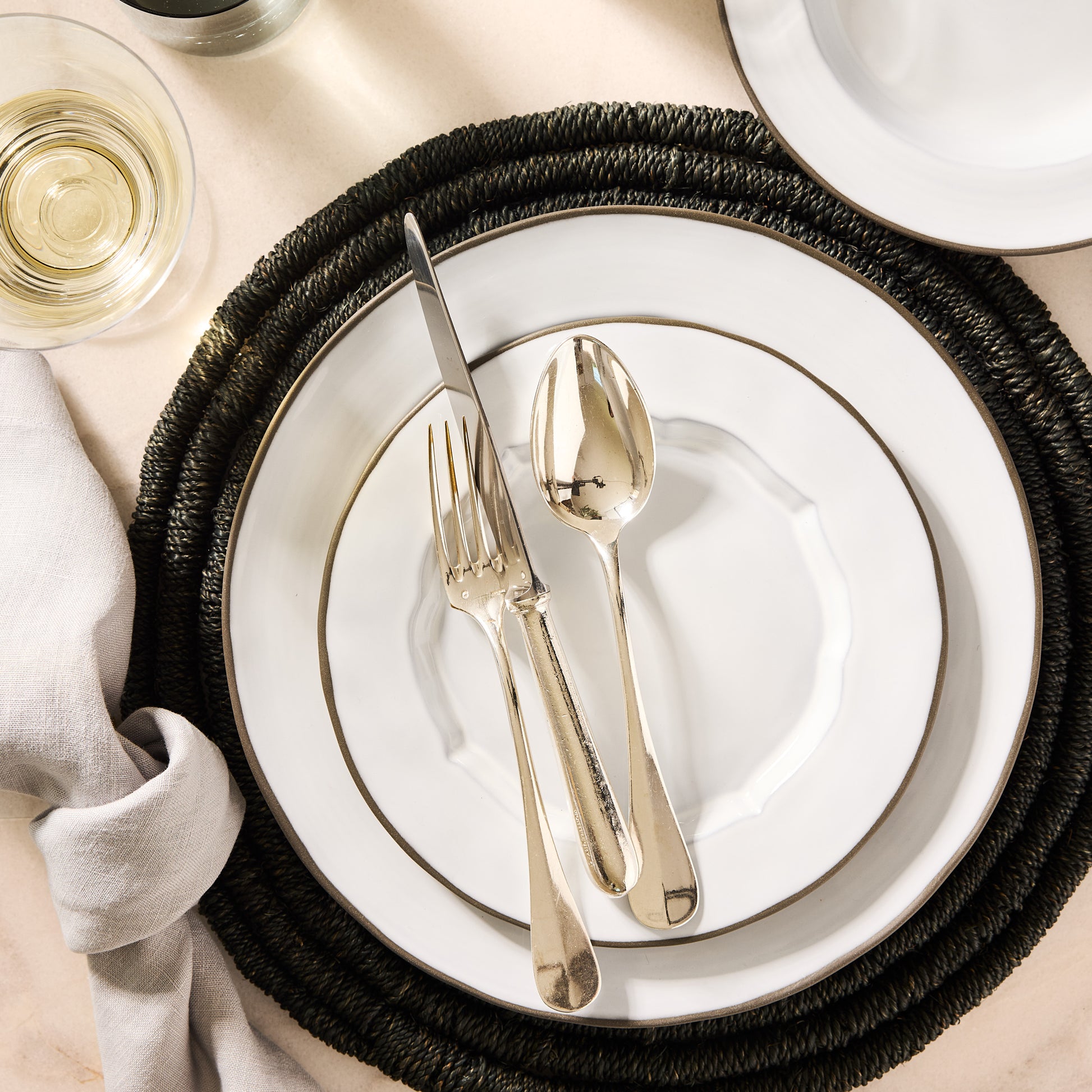 White dinner plate with gold rim, silver cutlery, and dark woven placemat.