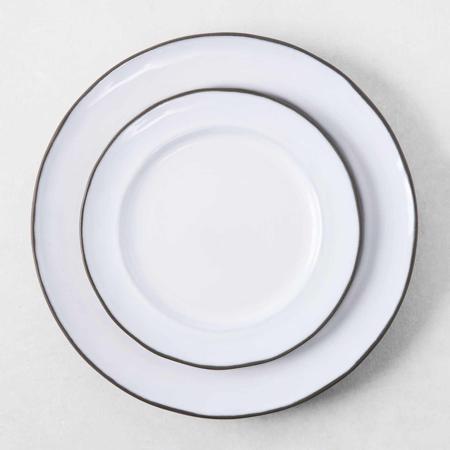 Two white enamelware plates with dark rims, stacked.