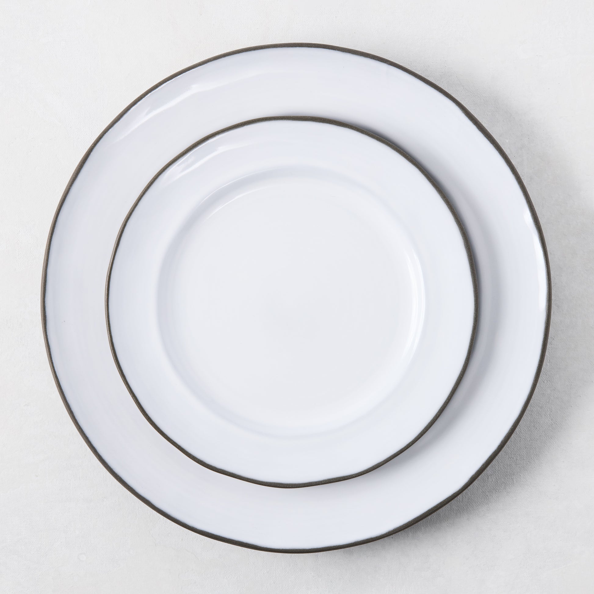 Two white enamelware plates with dark rims, stacked.