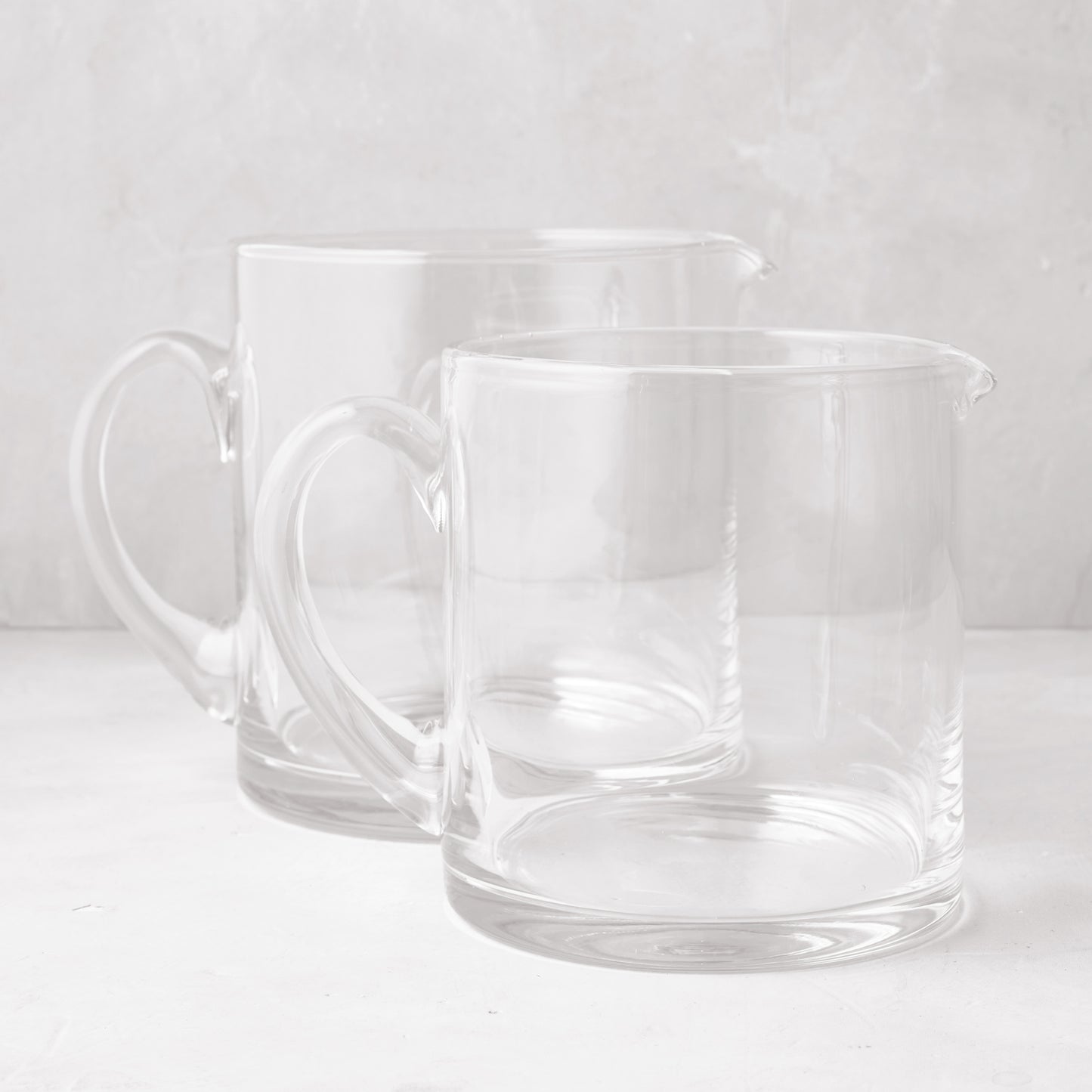 Two clear, hand-blown glass Soho Short Pitchers, one 40 oz and one 56 oz, with handles and spouts.