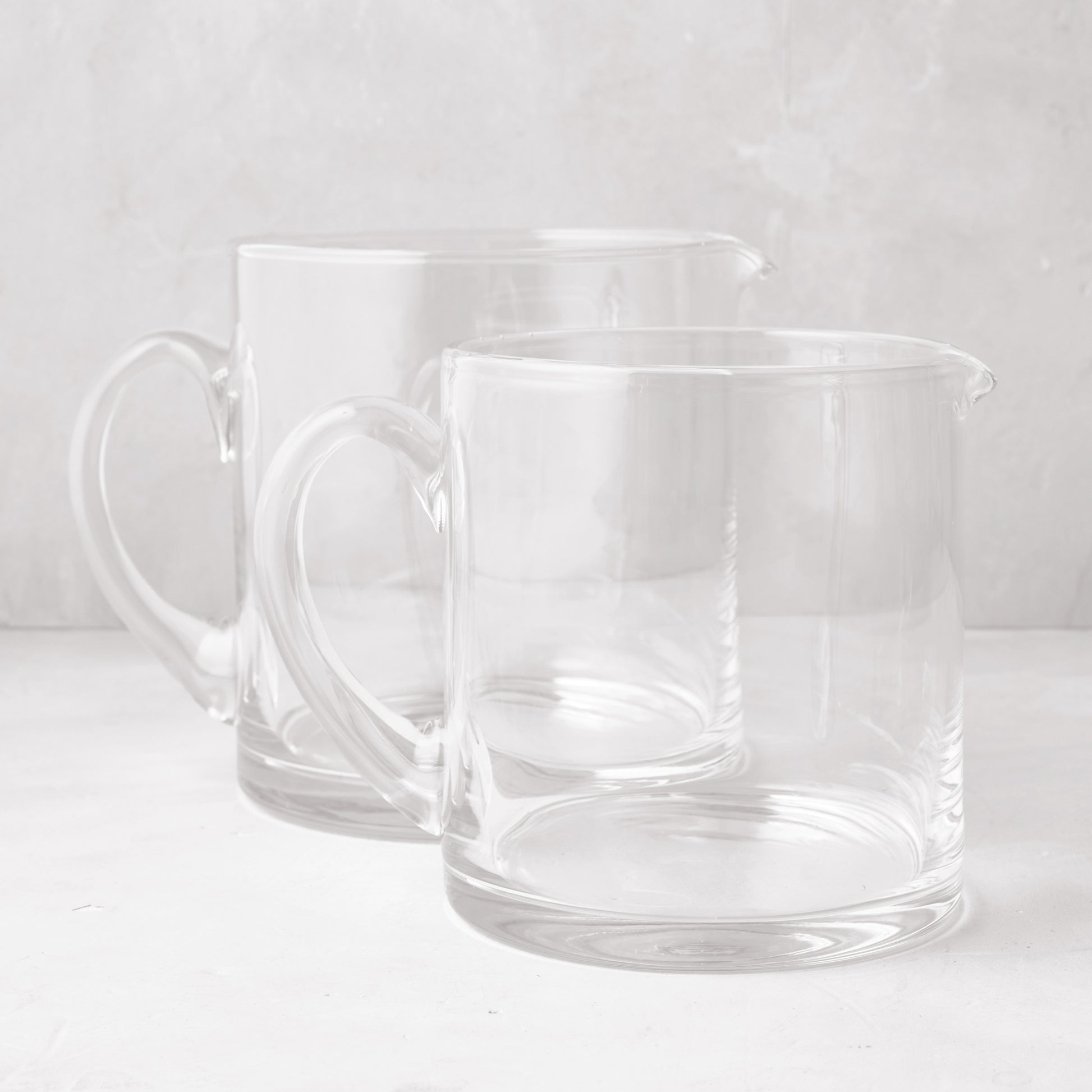 Two clear, hand-blown glass Soho Short Pitchers, one 40 oz and one 56 oz, with handles and spouts.
