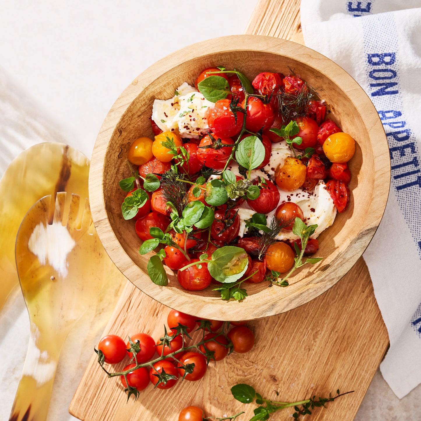Wooden bowl filled with roasted cherry tomatoes, fresh mozzarella, and herbs.
