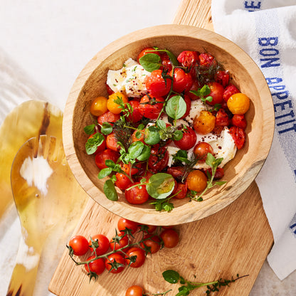 Wooden bowl filled with roasted cherry tomatoes, fresh mozzarella, and herbs.
