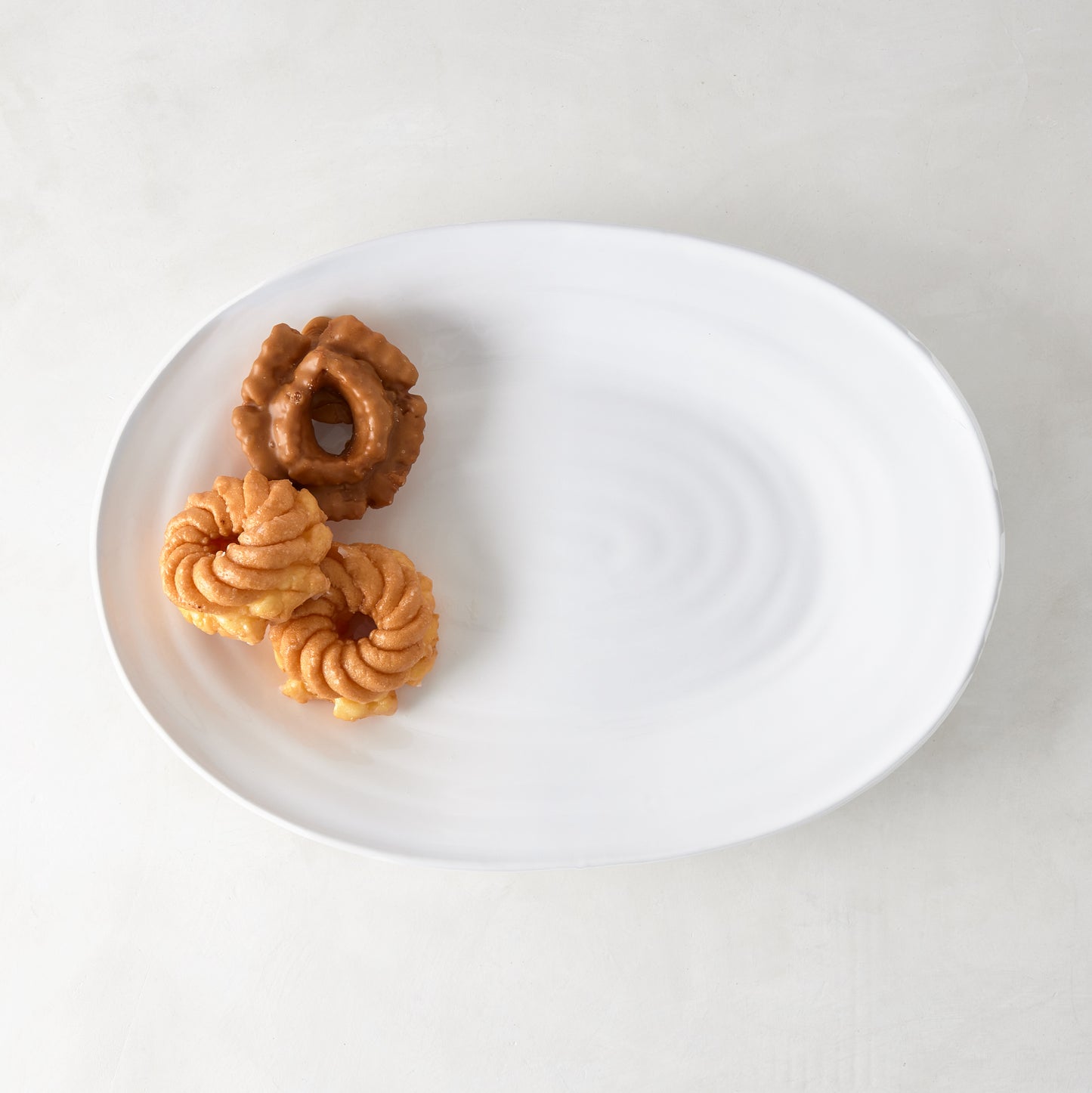 White ceramic oval serving platter with a subtle spiral design, holding two glazed pastries.