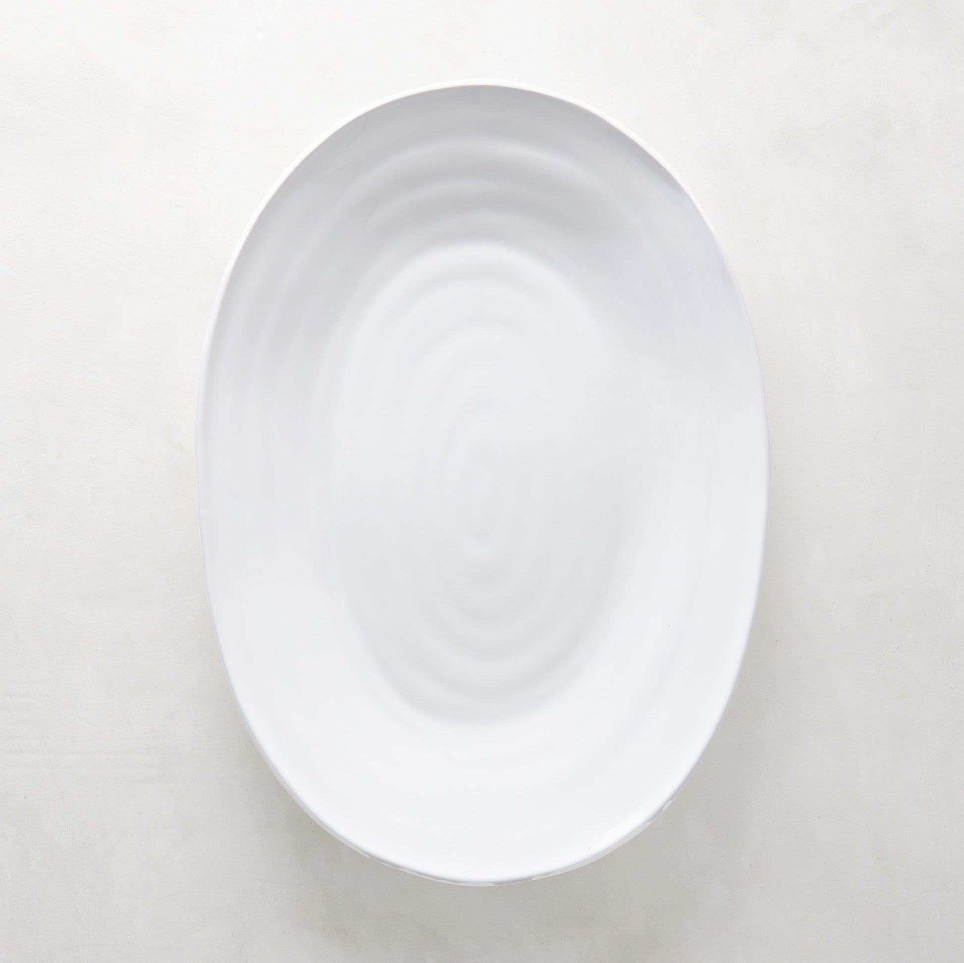 White ceramic oval serving platter with a subtle spiral design, 17"L x 12.5"W.