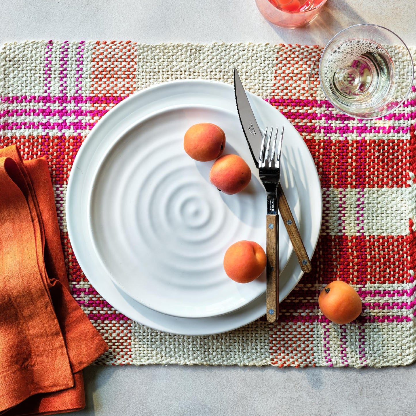 Handmade white ceramic 9-inch salad plate with a spiral texture, set on a colorful woven placemat with apricots and cutlery.