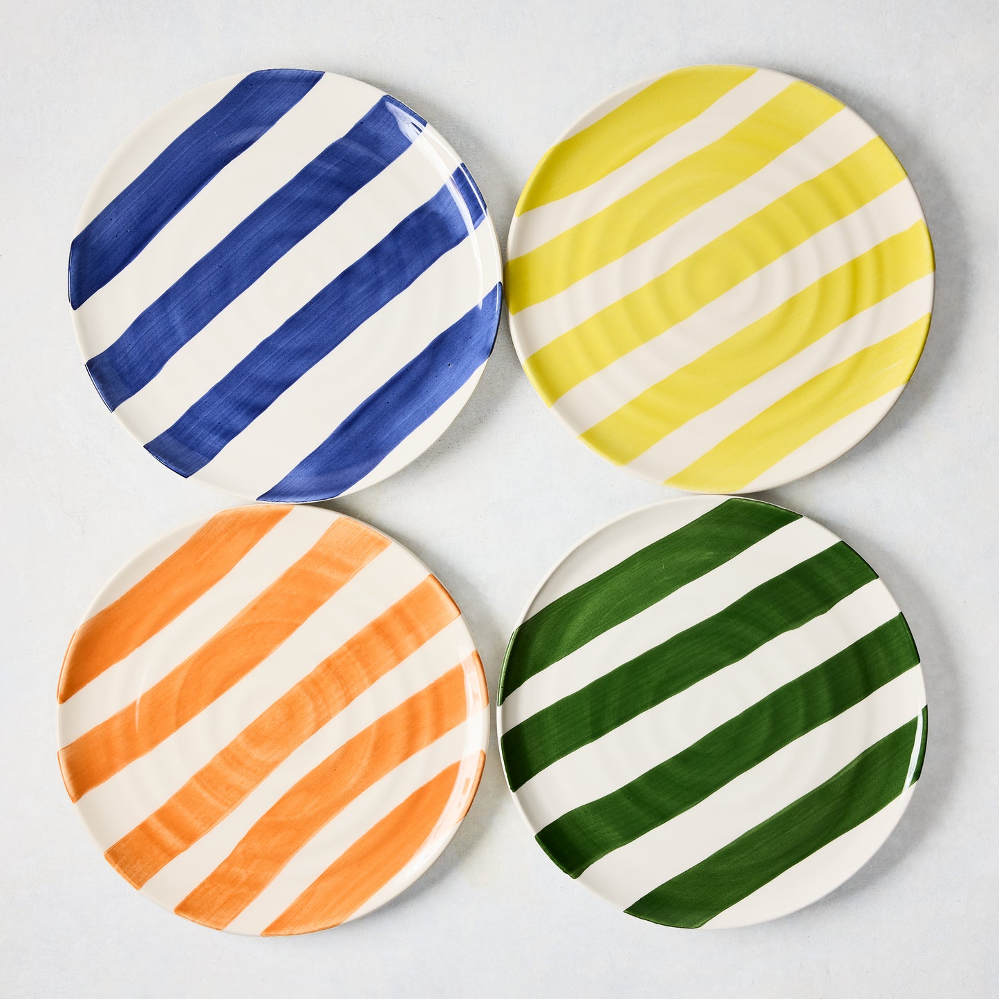 Four 9" ceramic salad plates with hand-painted diagonal stripes in blue, yellow, orange, and green.