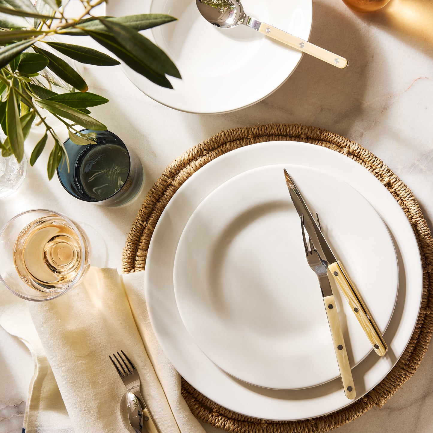 Round natural woven abaca placemat, 15" Dia, under white plates with cutlery.