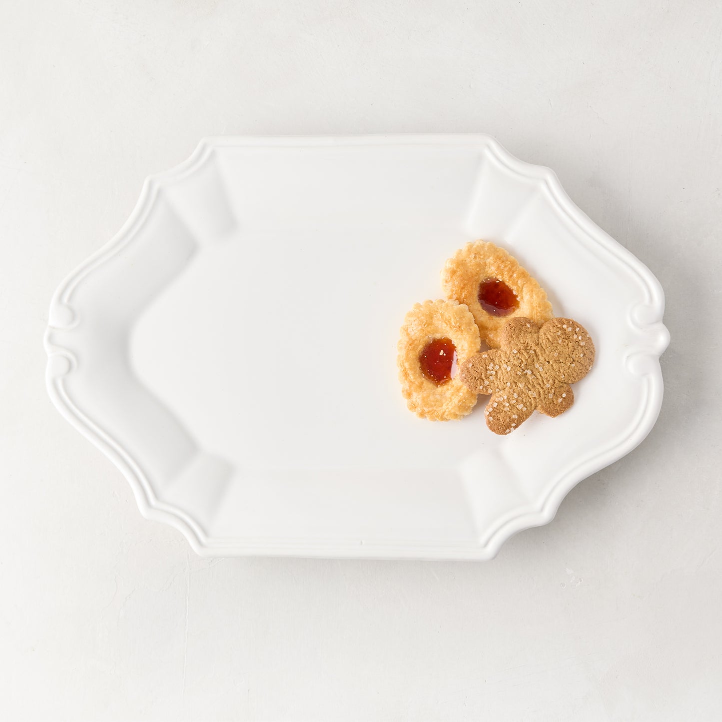 White Sprezzatura ceramic serving platter with detailed edges, holding three cookies.