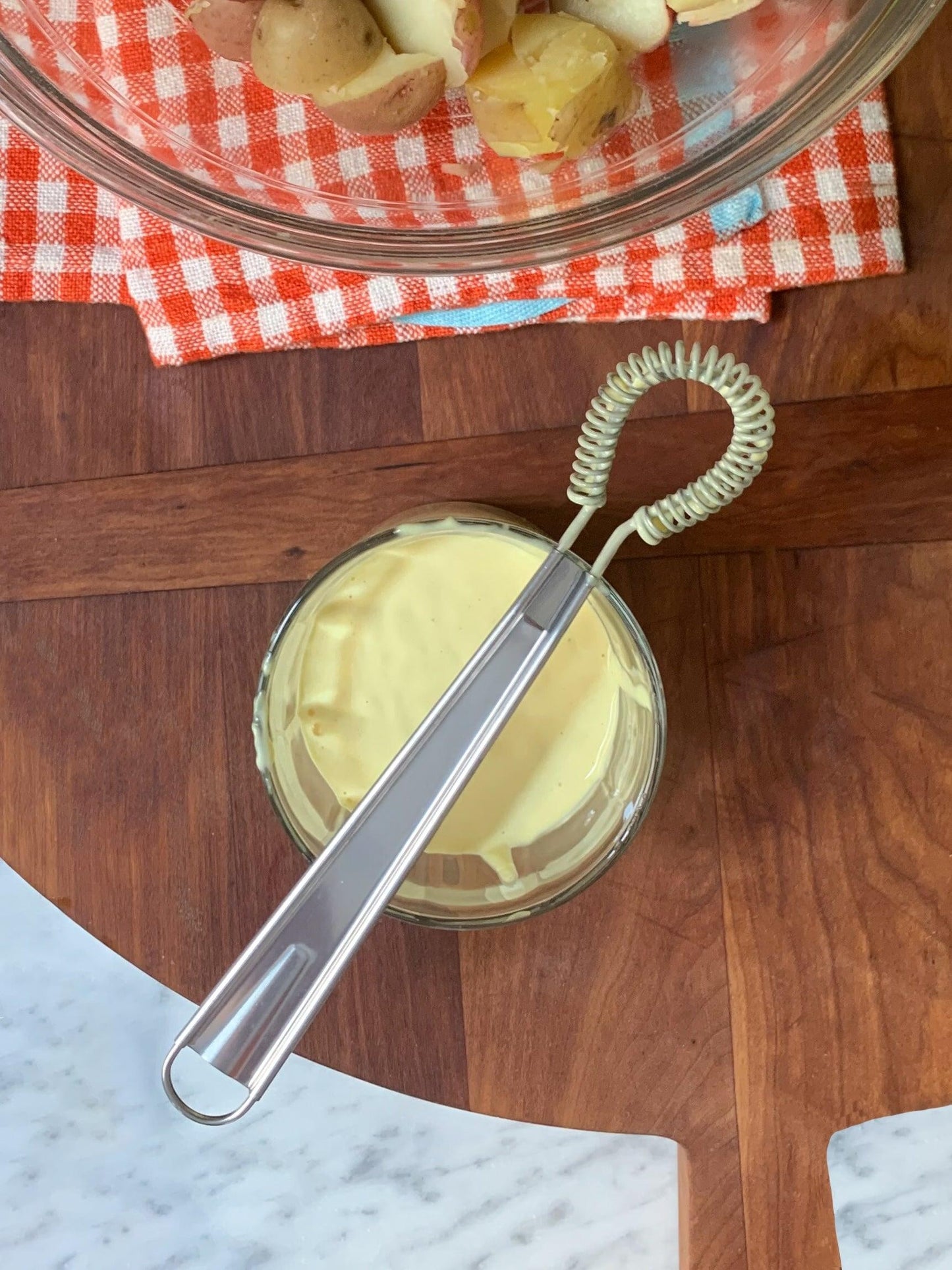 Stainless steel mini whisk with a coiled head resting in a glass of yellow sauce.