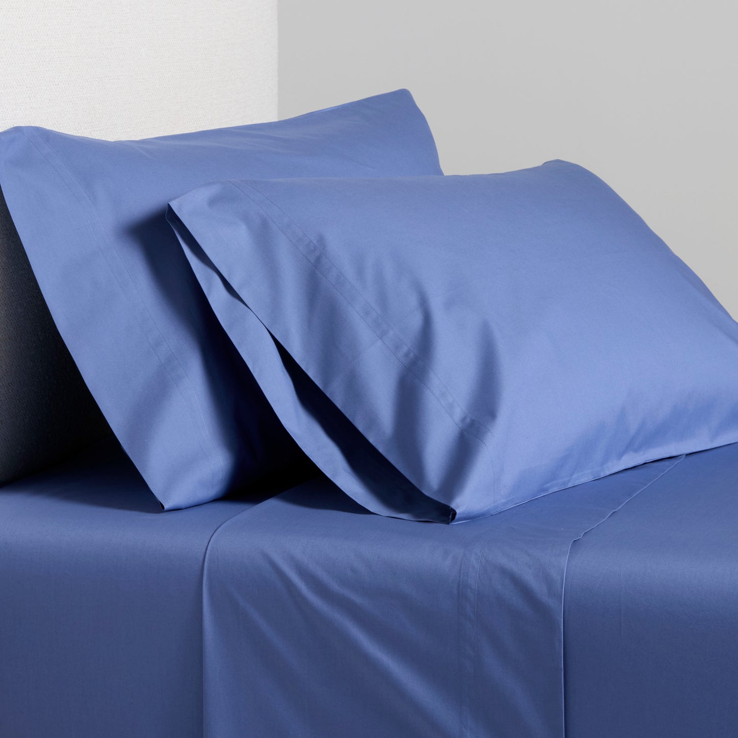 Steele Blue Italian Percale Sheet Set with two pillowcases and flat sheet on a bed.