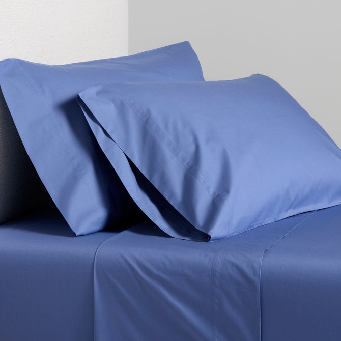 Steele Blue Italian Percale Sheet Set with two pillowcases and flat sheet on a bed.
