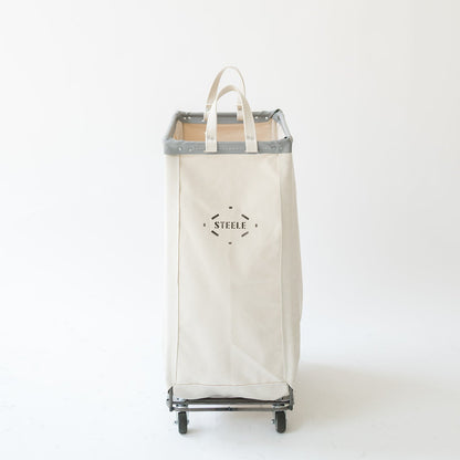 Tall off-white cotton canvas caddie with a steel frame, grey trim, and rolling wheels, featuring the Steele logo.