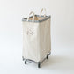 Tall Steele canvas caddie in natural cotton with a steel frame, grey trim, and rolling caster wheels on a white background.