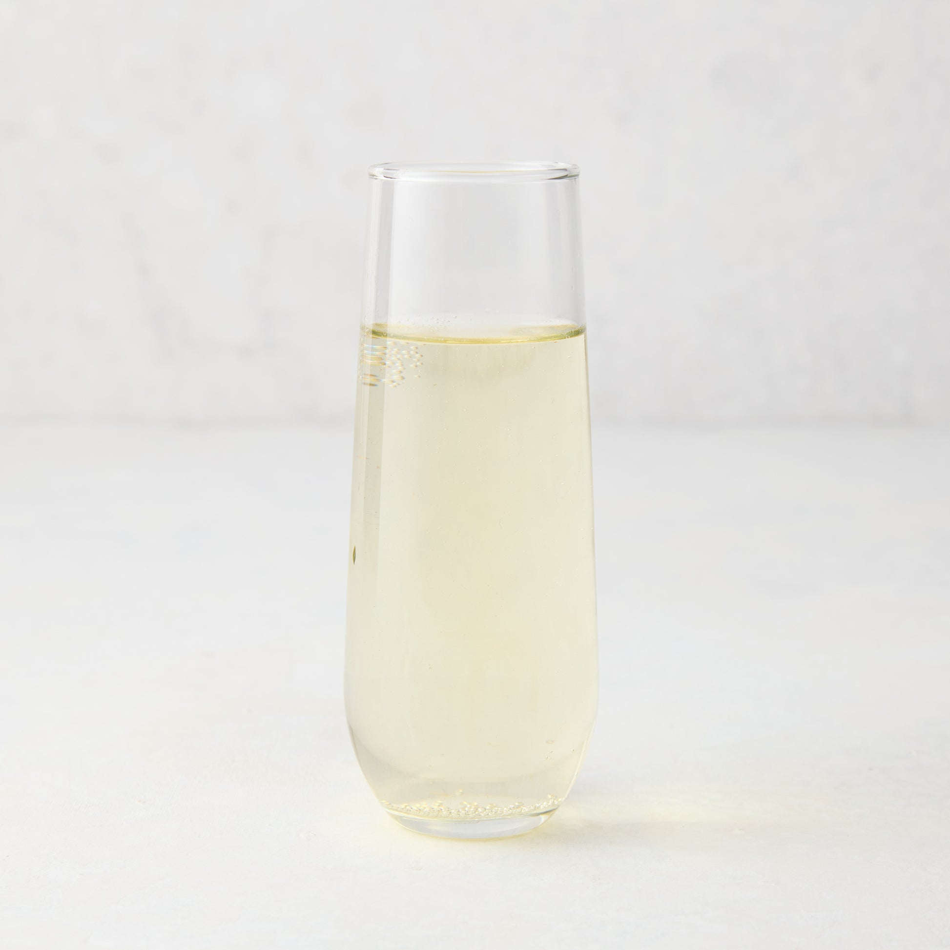 Clear Hudson Grace stemless champagne flute with sparkling light yellow liquid.