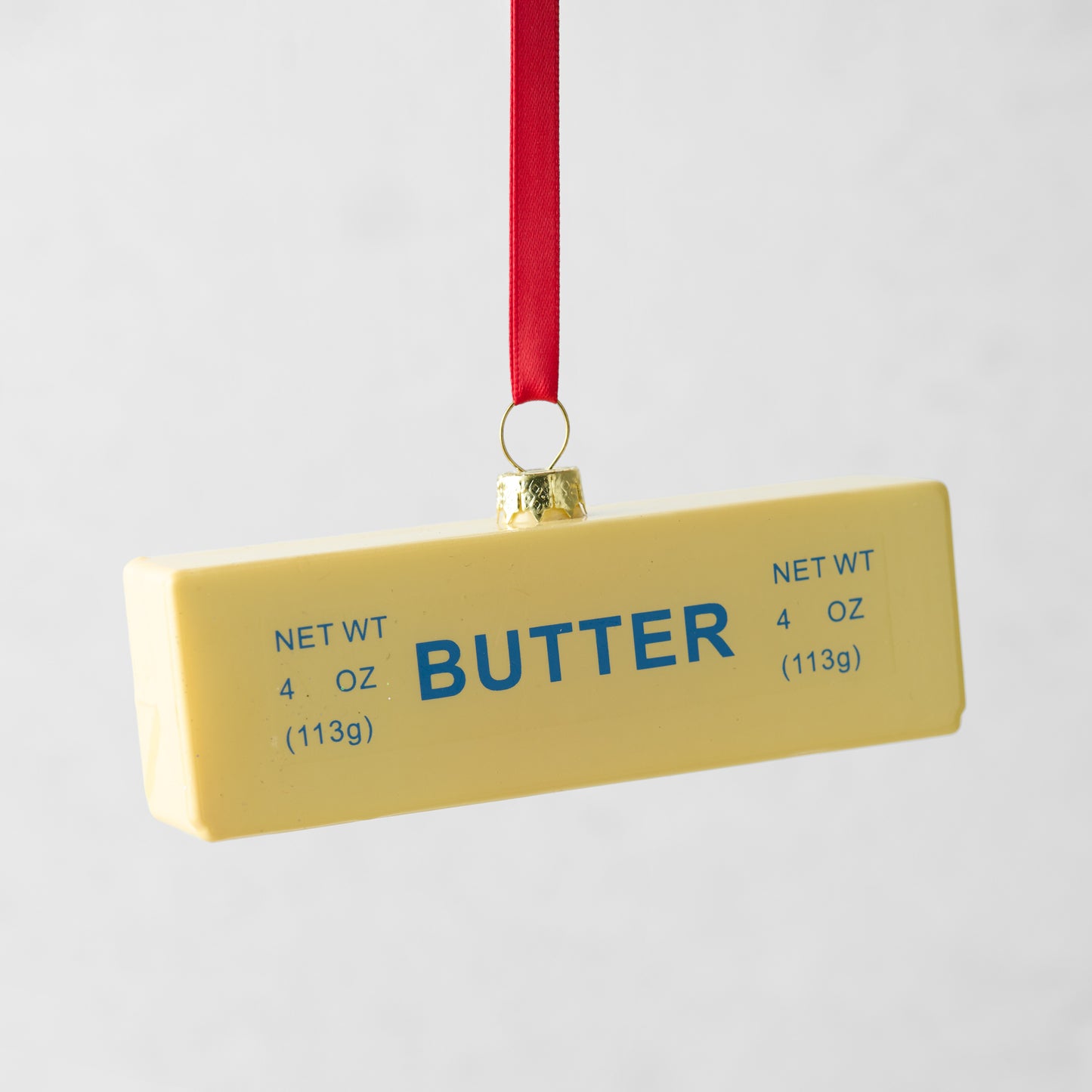 Yellow glass stick of butter Christmas tree ornament with blue "BUTTER" text and red ribbon.