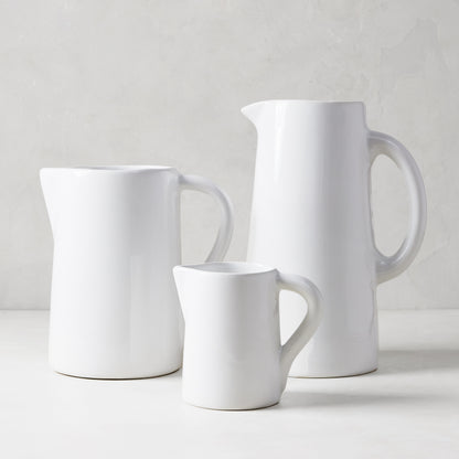 Three handmade white ceramic Stinson pitchers in small, medium, and large sizes, with handles and spouts.