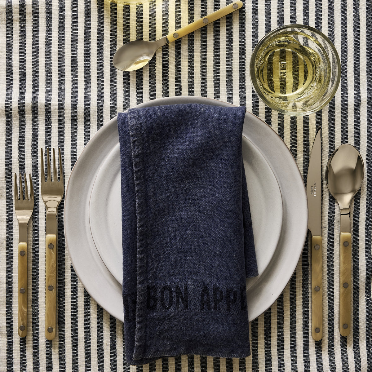 10.75-inch stone grey glazed terracotta dinner plate topped with a navy blue napkin on a striped tablecloth.