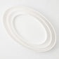 Three nested, oval-shaped white stoneware platters with a smooth, minimalist design on a light background.