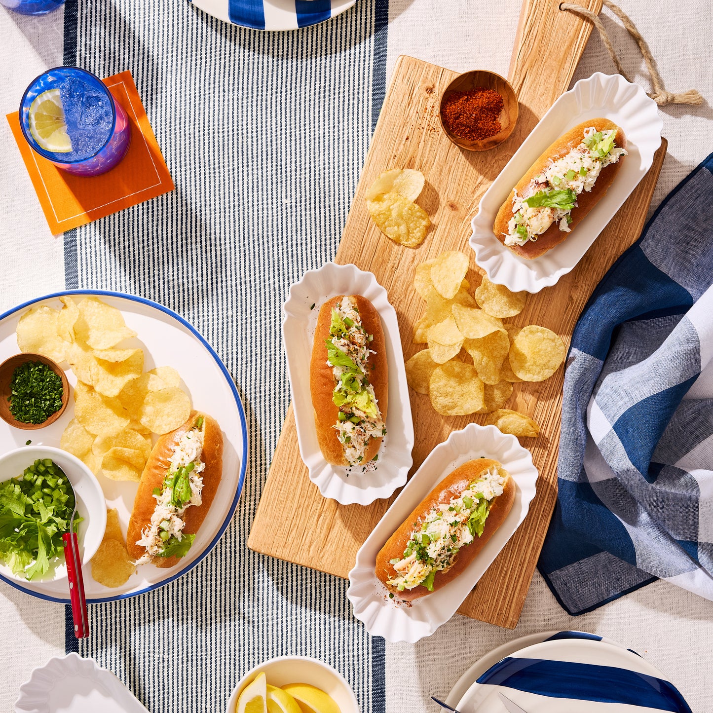 White Melamine Street Eats Hot Dog Holder with lobster rolls and chips on a striped tablecloth.