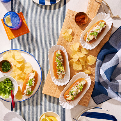 White Melamine Street Eats Hot Dog Holder with lobster rolls and chips on a striped tablecloth.