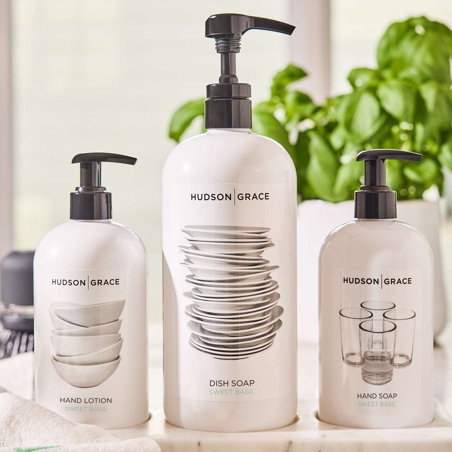 Three white Hudson Grace Sweet Basil bottles: dish soap (32 oz), hand lotion, and hand soap, with black pumps.