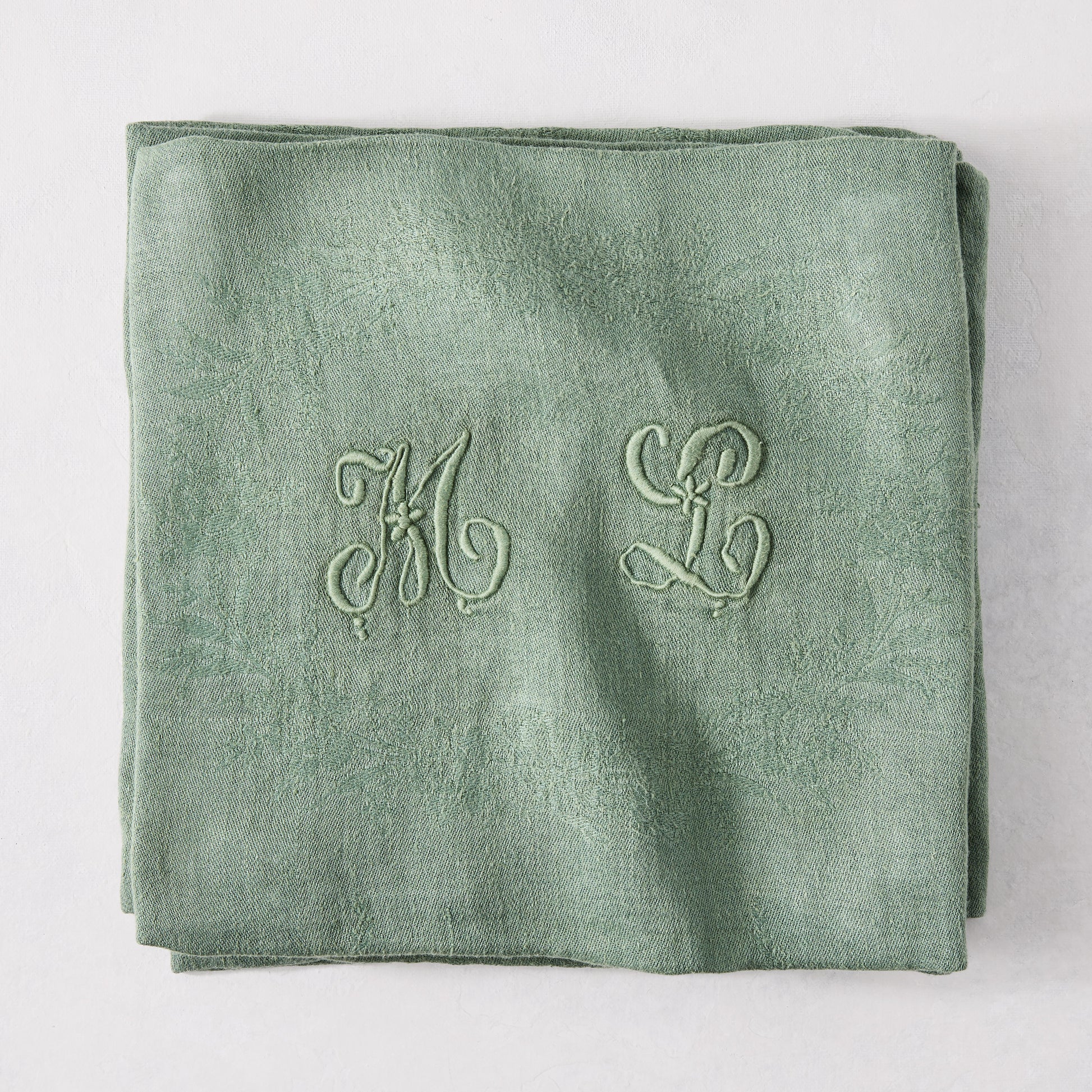 Folded Swiss Chard green antique French monogram napkin, linen-cotton blend, with embroidered "ML" initials.