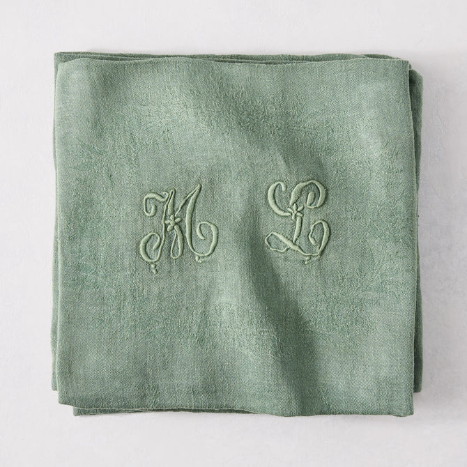 Folded Swiss Chard green antique French monogram napkin, linen-cotton blend, with embroidered "ML" initials.