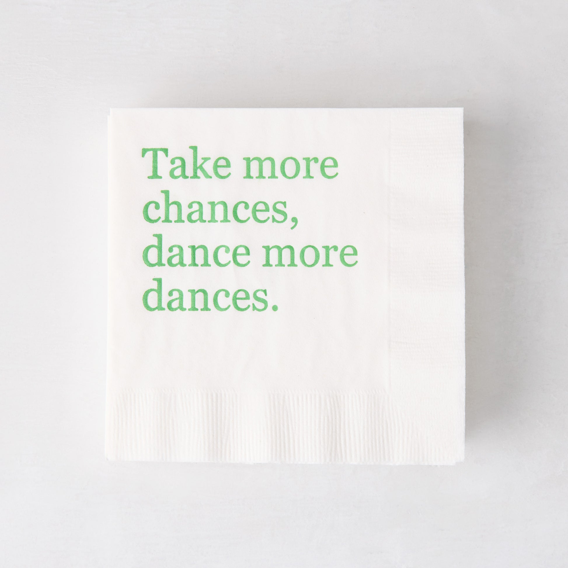 White 3-ply paper cocktail napkin with "Take more chances, dance more dances" in green text.