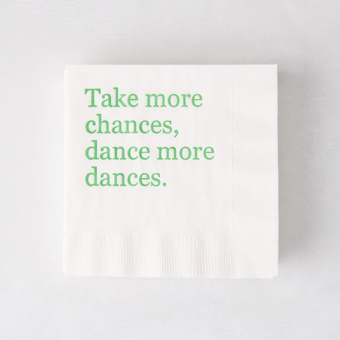 White 3-ply paper cocktail napkin with "Take more chances, dance more dances" in green text.