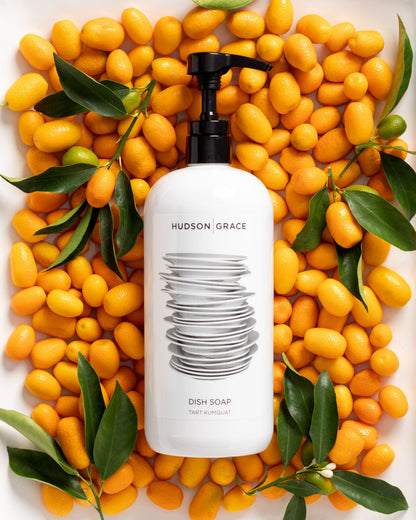 White HG Tart Kumquat Dish Soap bottle with a black pump, surrounded by kumquats and green leaves.